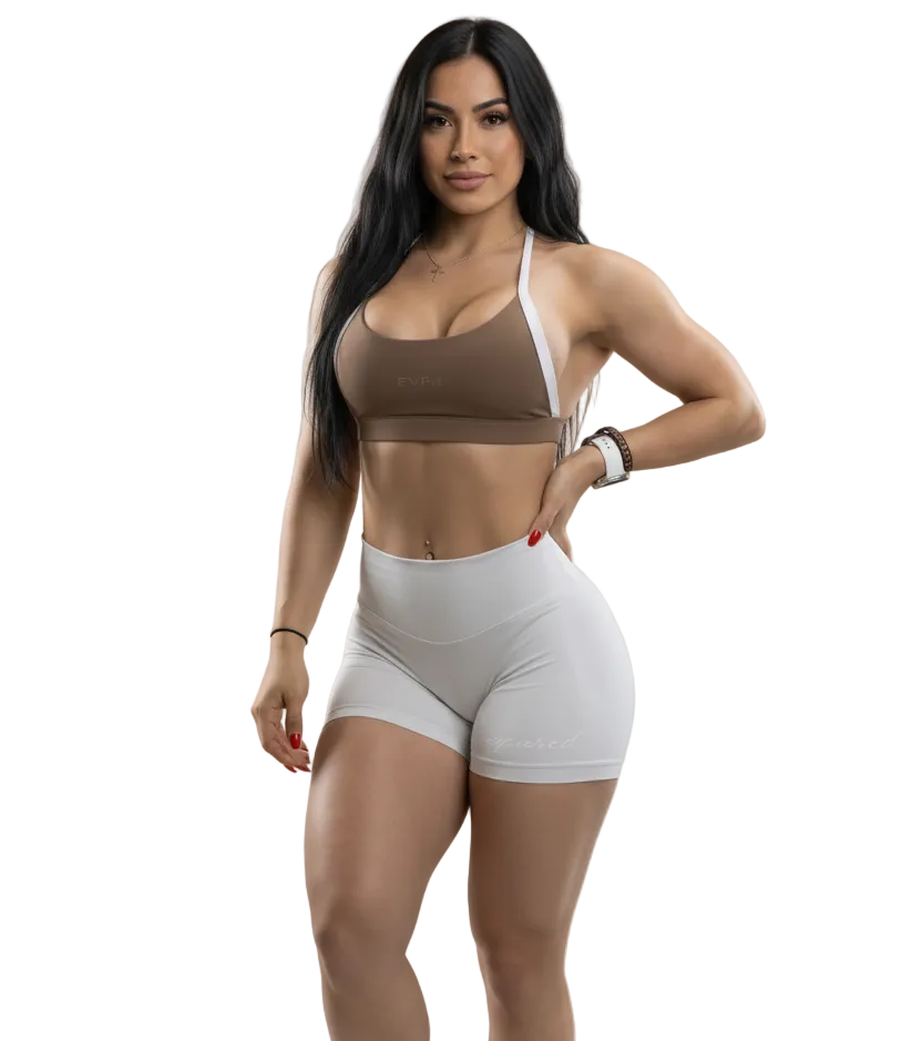 Woman wearing a brown sports bra and white shorts on a gray background
