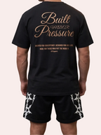 Man wearing a black t-shirt with 'Built Under Pressure' text in a warehouse with stacks of money on fire.
