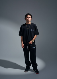 Person wearing a black outfit with a logo on a gray background