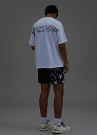 Person wearing a white t-shirt with text and black shorts with white patterns on a gray background