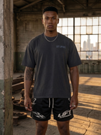 Man wearing a dark gray 'LIFT APPAREL' t-shirt and black shorts in an industrial setting.
