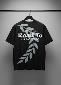 Black t-shirt with white text and leaf design on a hanger against a gray background