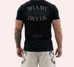 Person wearing a black t-shirt with 'MIAMI FLORIDA IN VIVO' text, standing on an urban street.