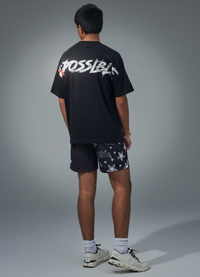 Person wearing a black t-shirt with white text and patterned shorts on a gray background
