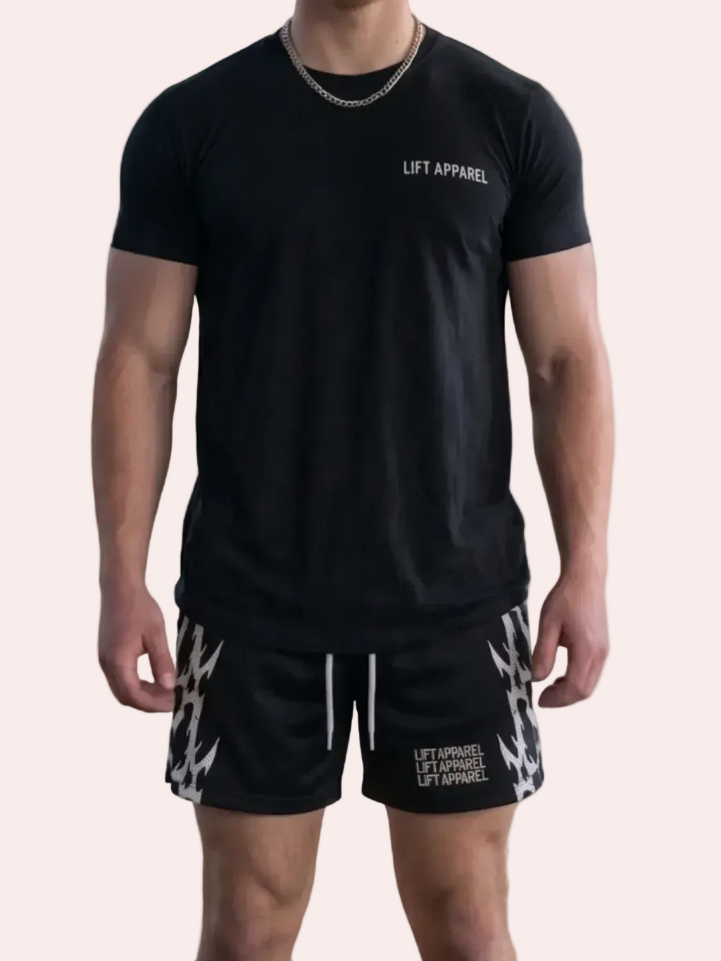 Man wearing a black t-shirt and patterned shorts standing in an industrial setting with graffiti.