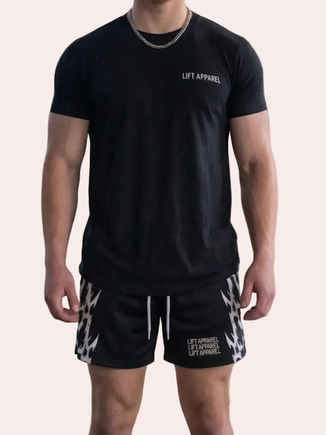 Man wearing a black t-shirt and patterned shorts standing in an industrial setting with graffiti.