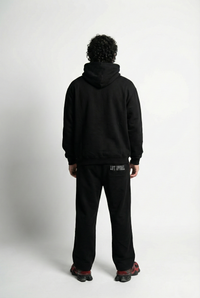 Person wearing a black hoodie and pants on a white background