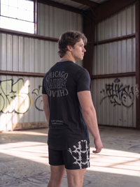 Person wearing a black t-shirt with 'Chicago' text in an urban setting with graffiti.
