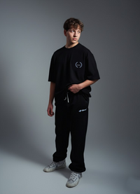 Person wearing a black t-shirt and pants with a logo on a gray background
