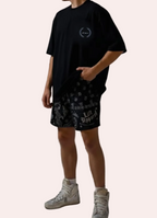 Person wearing a black t-shirt and patterned shorts on a gray background