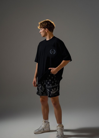 Person wearing a black t-shirt and patterned shorts on a gray background