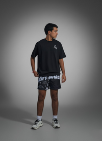 Person wearing a black t-shirt and patterned shorts on a gray background