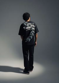 Person wearing a black t-shirt with text and graphics on the back, standing against a gray background