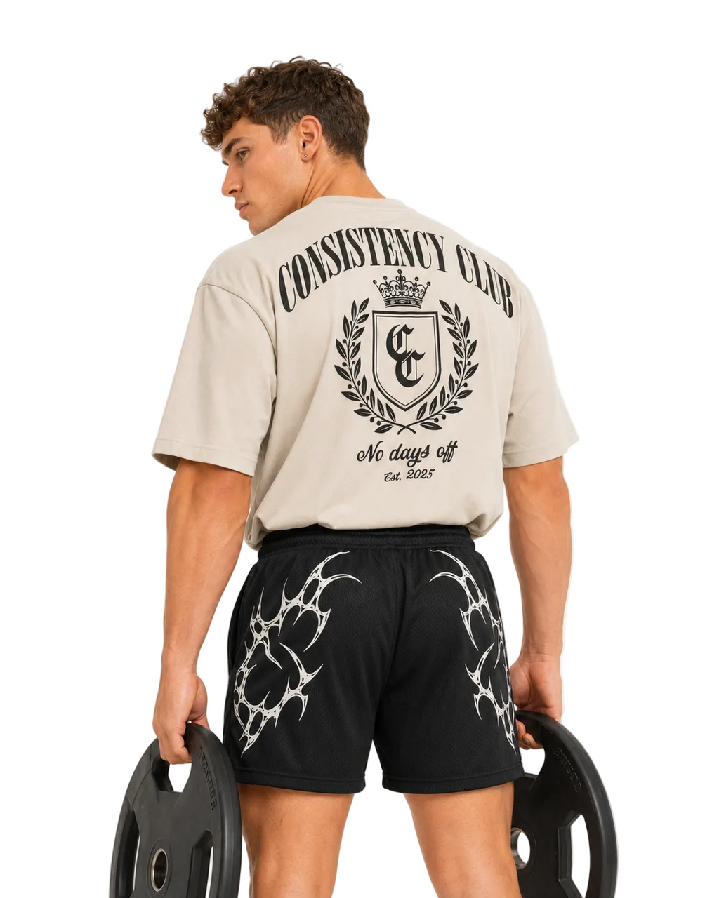 Man holding a weight plate wearing black Apex gym shorts and a cream oversized tee