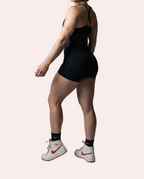 Woman in black athletic outfit with white sneakers on a gray background