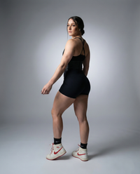 Woman in black athletic outfit with white sneakers on a gray background