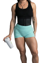 Woman wearing a black tank top and light blue shorts holding a white bottle on a gray background