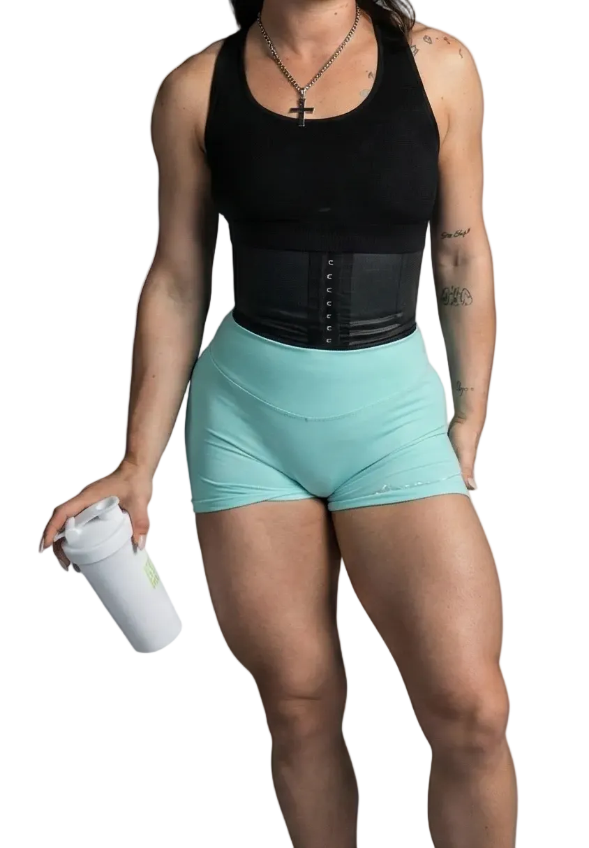 Woman wearing a black tank top and light blue shorts holding a white bottle on a gray background