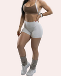 Woman wearing a brown sports bra and white shorts on a gray background