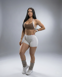 Woman wearing a brown sports bra and white shorts on a gray background