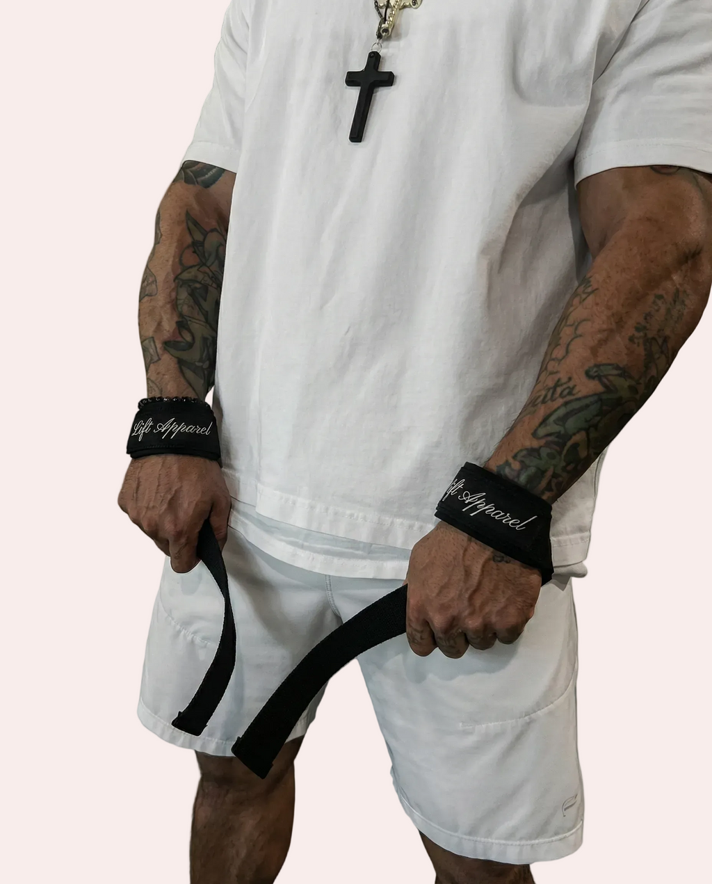 Person wearing a white outfit with tattoos and a cross necklace, holding a black belt.