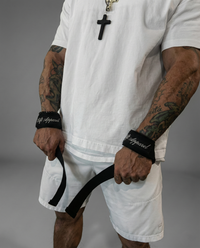 Person wearing a white outfit with tattoos and a cross necklace, holding a black belt.